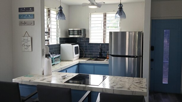 A modern kitchen with a marble countertop, a stainless steel refrigerator, and a microwave. There are two pendant lights and a ceiling fan. - 2-bedroom house in peaceful Lower Carlton w/ AC, WiFi. Within steps of the beach (Lower Carlton)