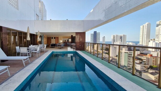 A rooftop pool with lounge chairs and a dining area, offering a city view. - COGRA0102 - Edifício Graça Prime (Salvador)