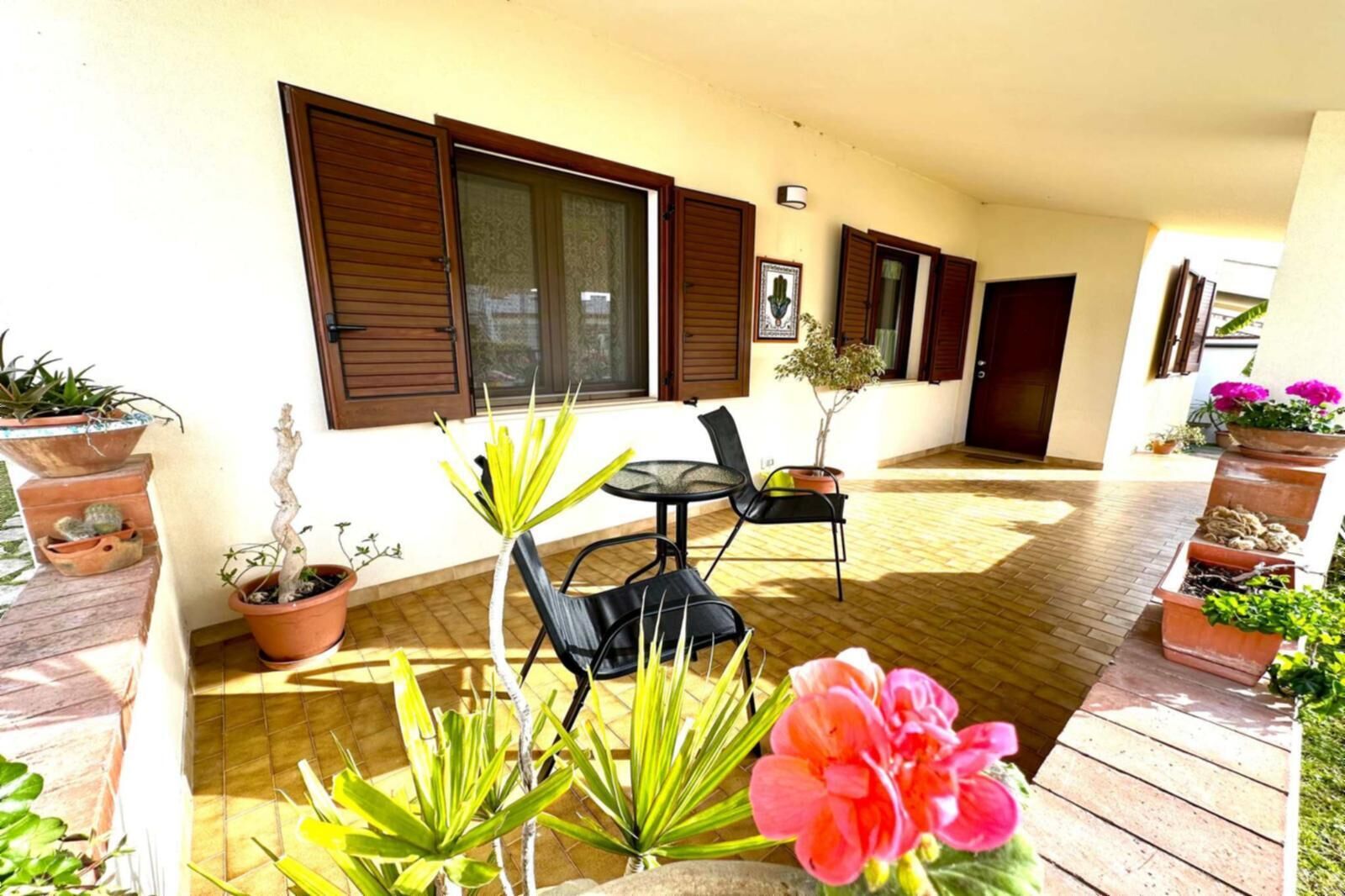 An outdoor patio with a table and chairs, surrounded by potted plants and a wooden deck.