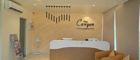 A reception area with a wooden reception desk, a reception sign, a fan, and a couch.