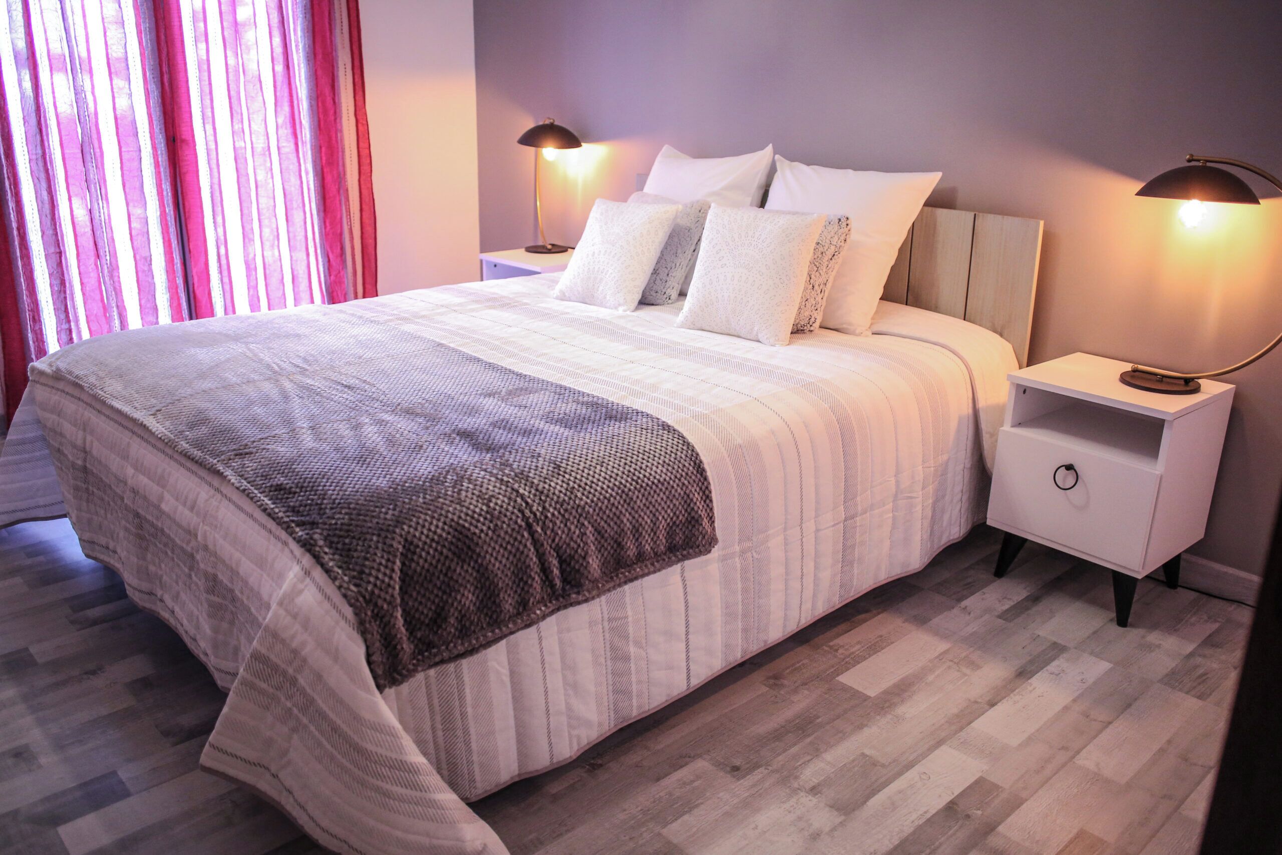 A neatly made bed with a striped blanket, two bedside lamps, and a nightstand with a drawer.