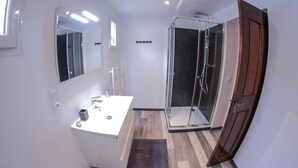 Une salle de bain moderne avec un meuble-lavabo blanc, une cabine de douche en verre et une porte en bois.