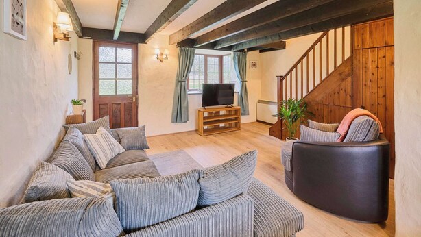 A cozy living room with a wooden staircase, a sofa set, and a television on a wooden stand. - Host & Stay | Providence Cottage (Woolacombe)