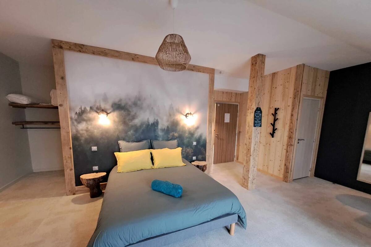Une chambre à coucher comprenant un lit, une table de chevet, une lampe fixée au mur et une tête de lit en bois.
