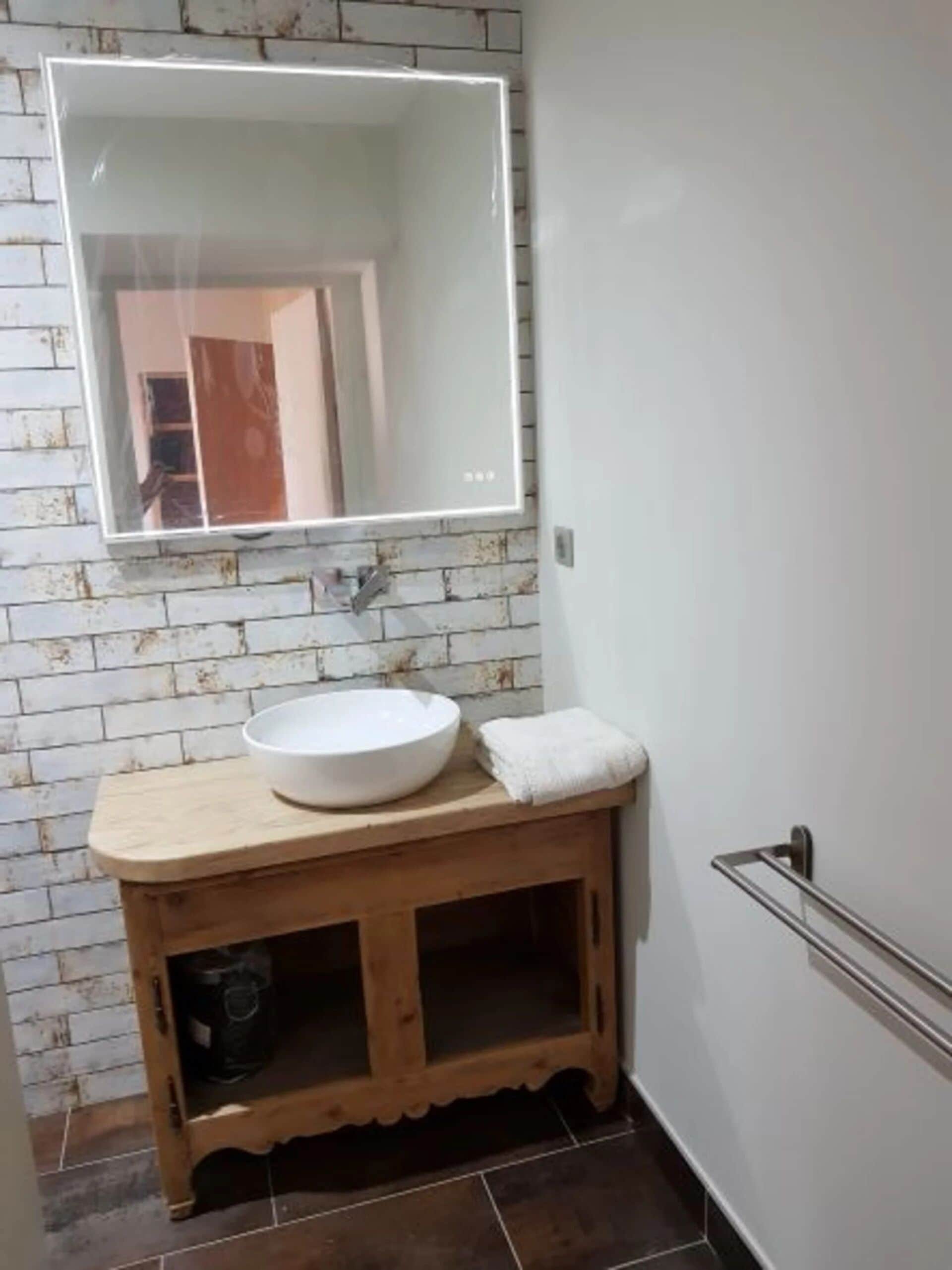 A bathroom with a white sink, wooden vanity, and a large mirror.