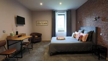 A bedroom with a bed, a desk, a chair, a TV, and a brick wall.