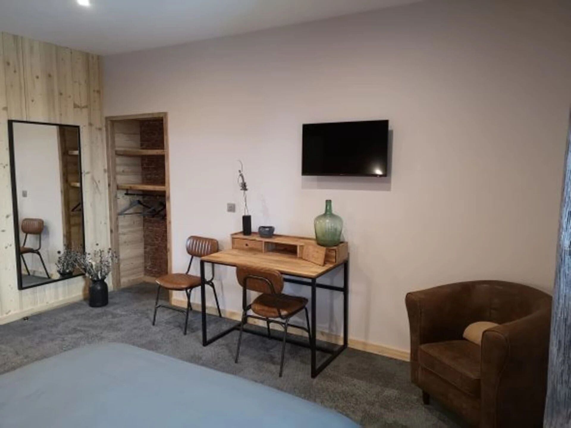 Una habitació amb un llit, una taula de treball amb dues cadires, una televisió i un butac armchair marró.