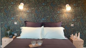 Ein Schlafzimmer mit gemustertem Wandpapier, einem Bett mit zwei Kissen, Nachttischen mit Dekoration und Wandleuchten.