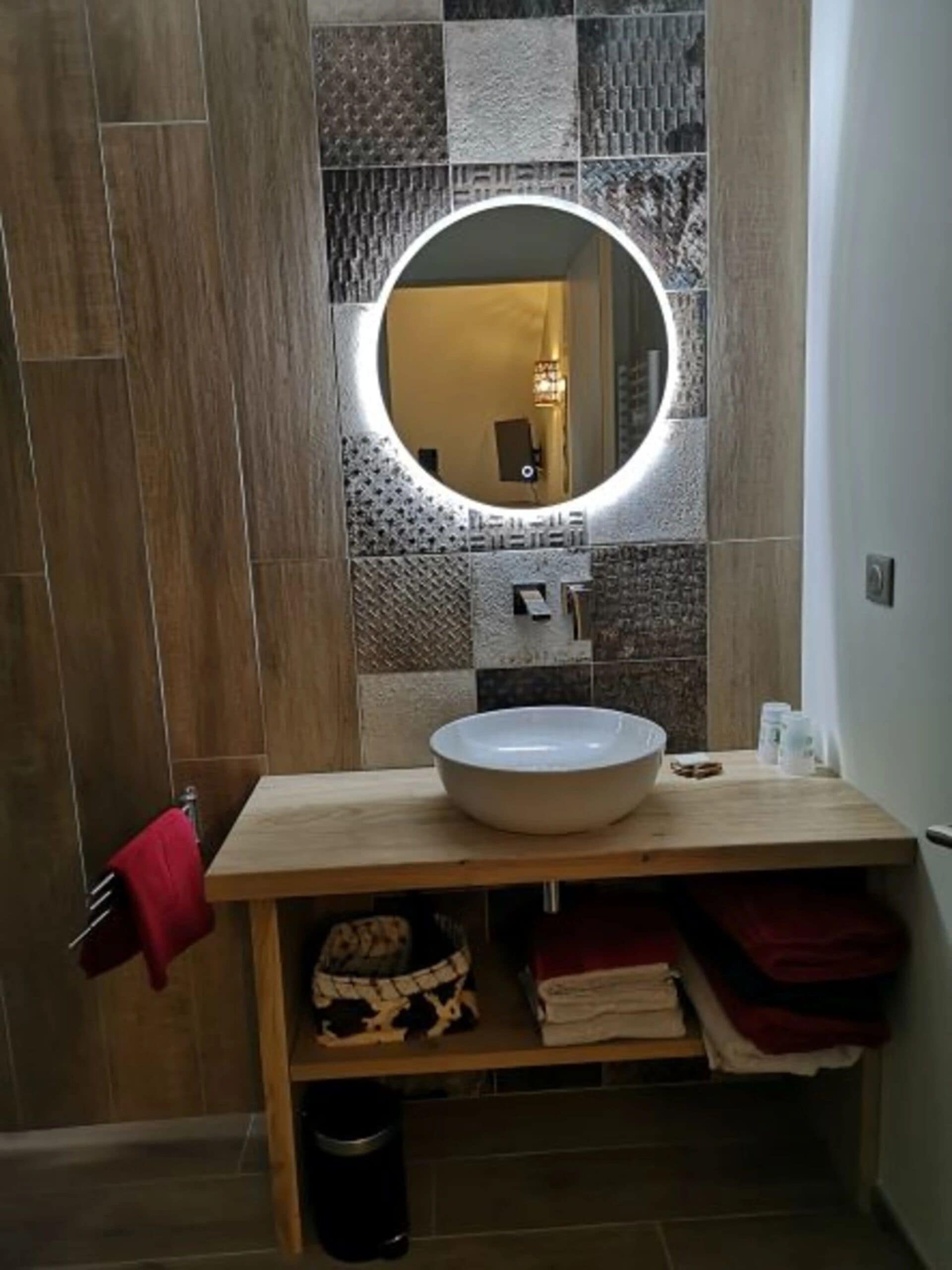 A bathroom with a round mirror, wooden vanity, and tiled walls.