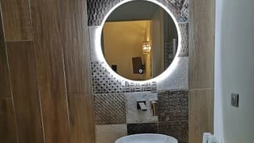 A bathroom with a round mirror, wooden vanity, and tiled walls.
