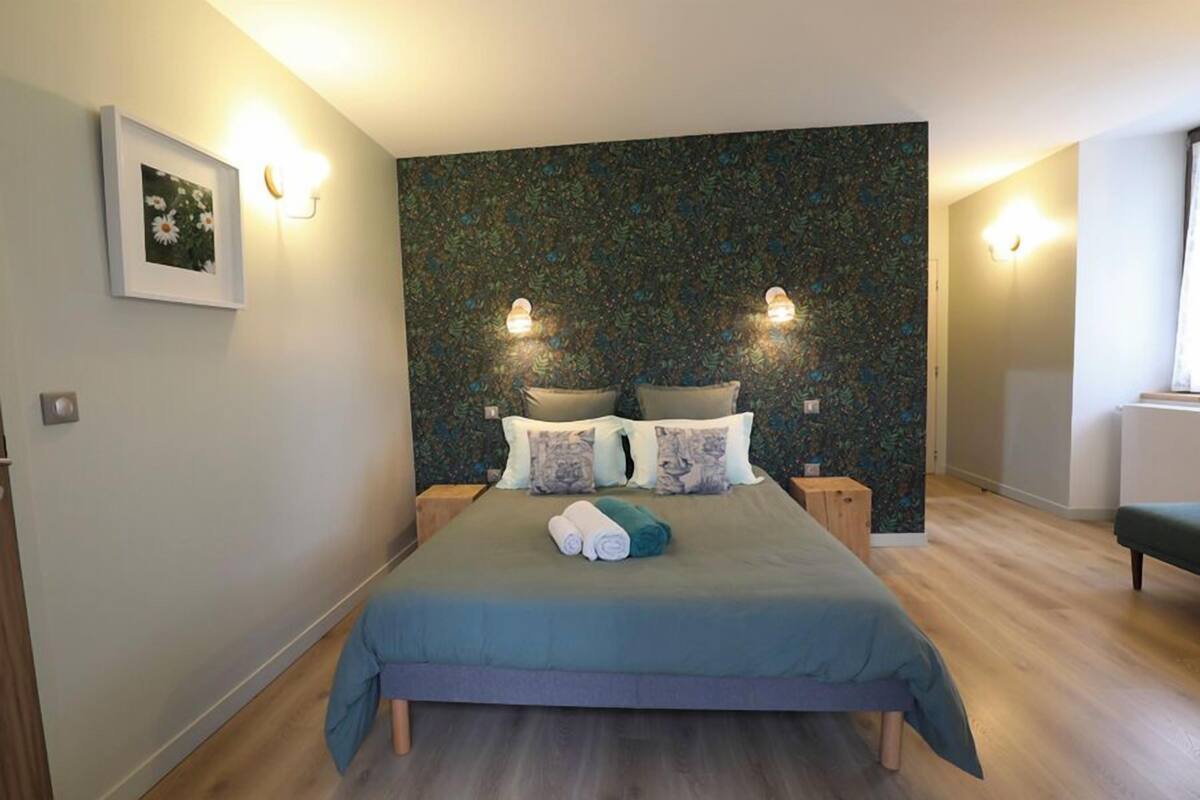 Une chambre moderne avec un grand lit, deux tables de chevet et un mur orné d’un motif floral.
