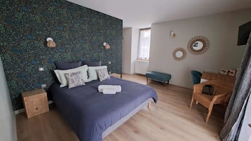Un dormitorio con una cama grande, una mesita de noche de madera, un escritorio pequeño y una silla de mimbre.