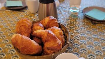 A table with a basket of croissants, a thermos, cups, and a plate with butter.