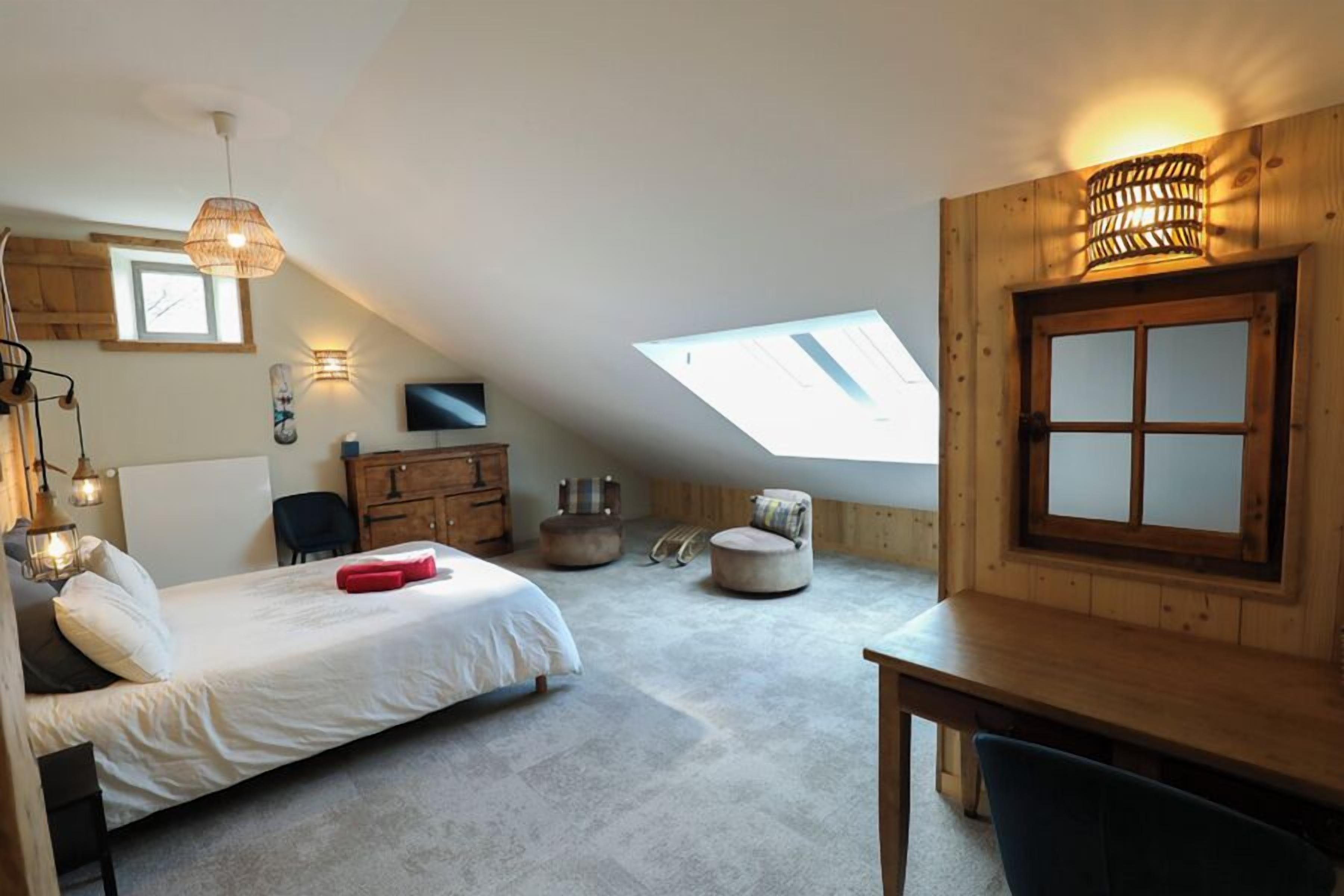 Een slaapkamer met een bed, een bureau, een stoel, een televisie, een raam en een houten wand.
