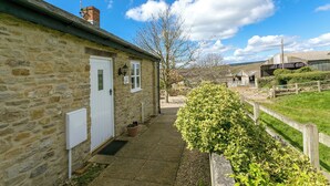 Un bâtiment en pierre avec une porte blanche, un petit jardin et un ciel dégagé.