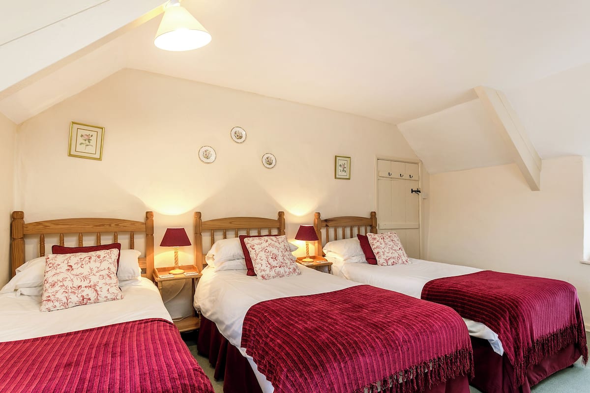 A bedroom with three beds, each with a red blanket and white bedding. There are bedside lamps and a ceiling light.