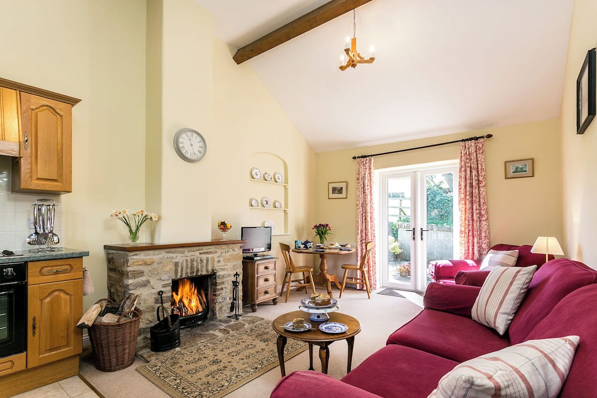 A cozy living room with a fireplace, a red sofa, a dining area with a table and chairs, and a kitchen with wooden cabinets.