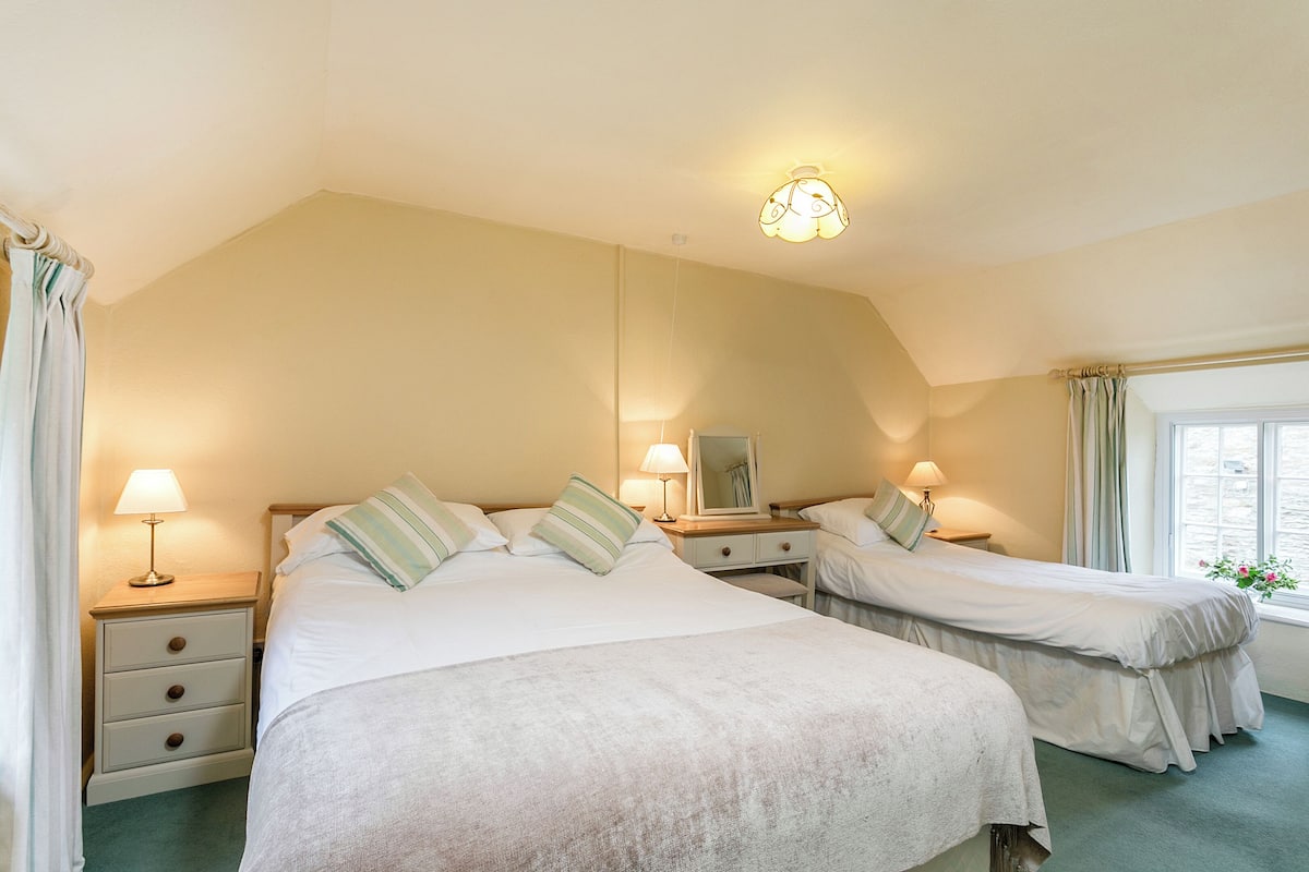 A room with two beds, a nightstand with a lamp, a mirror, and a window with curtains.