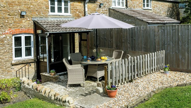 Une terrasse avec une table et des chaises, une clôture en bois et un mur en pierre.