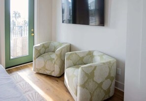 A room with two upholstered chairs, a large flat-screen TV mounted on the wall, and a sliding glass door leading to an outdoor area.