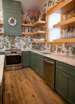 A kitchen with green cabinets, a wooden countertop, and a backsplash with tropical leaf patterns.