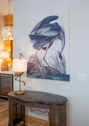 Una obra de arte en la pared con un pájaro, una mesa con lámpara y un candelabro.