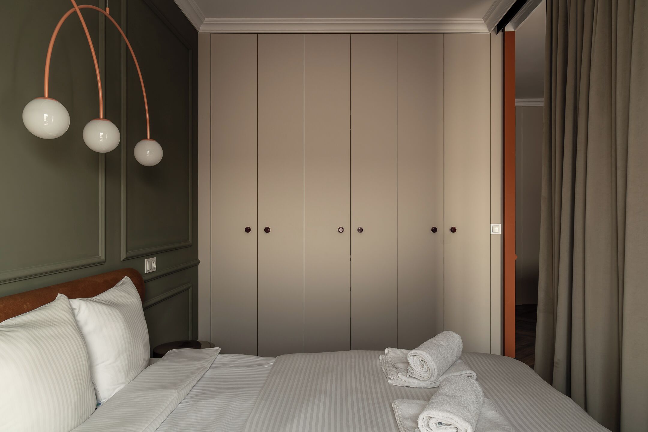 Un lit bien fait, avec des serviettes pliées, une tête de lit en bois et une armoire à deux portes.