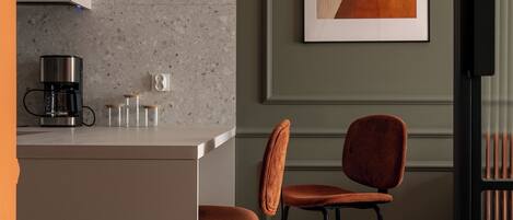 Una cocina moderna con una isla central, taburetes de bar, una cafetera y un cuadro abstracto en la pared.