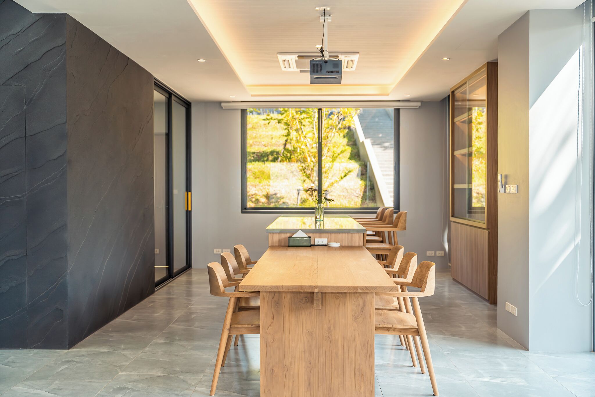 Una sala de conferencias moderna con una larga mesa de madera, sillas, un proyector y ventanas amplias que dan a zonas verdes.