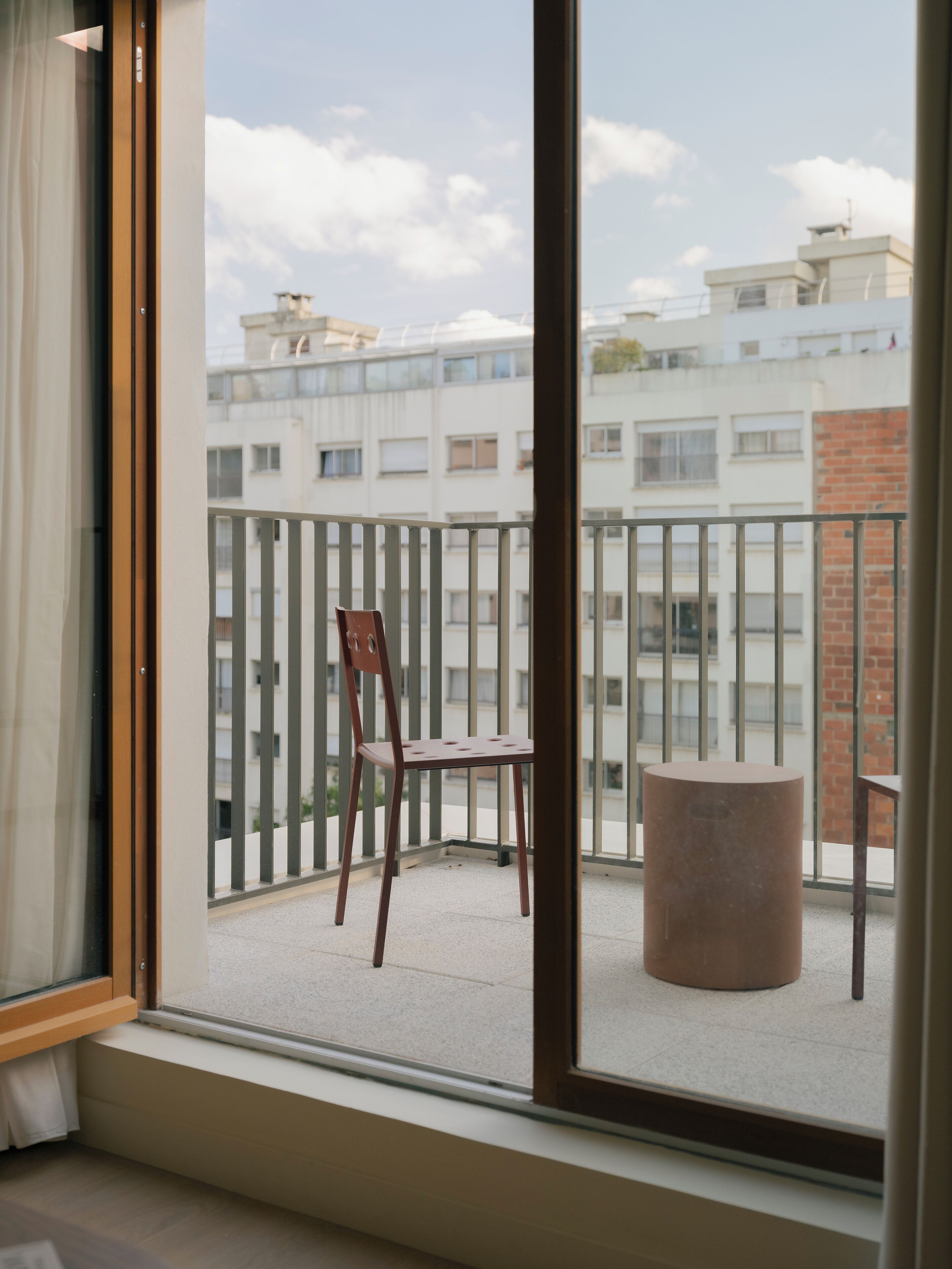 Un balcon avec une chaise et une table ronde, donnant sur un immeuble doté de nombreuses fenêtres.