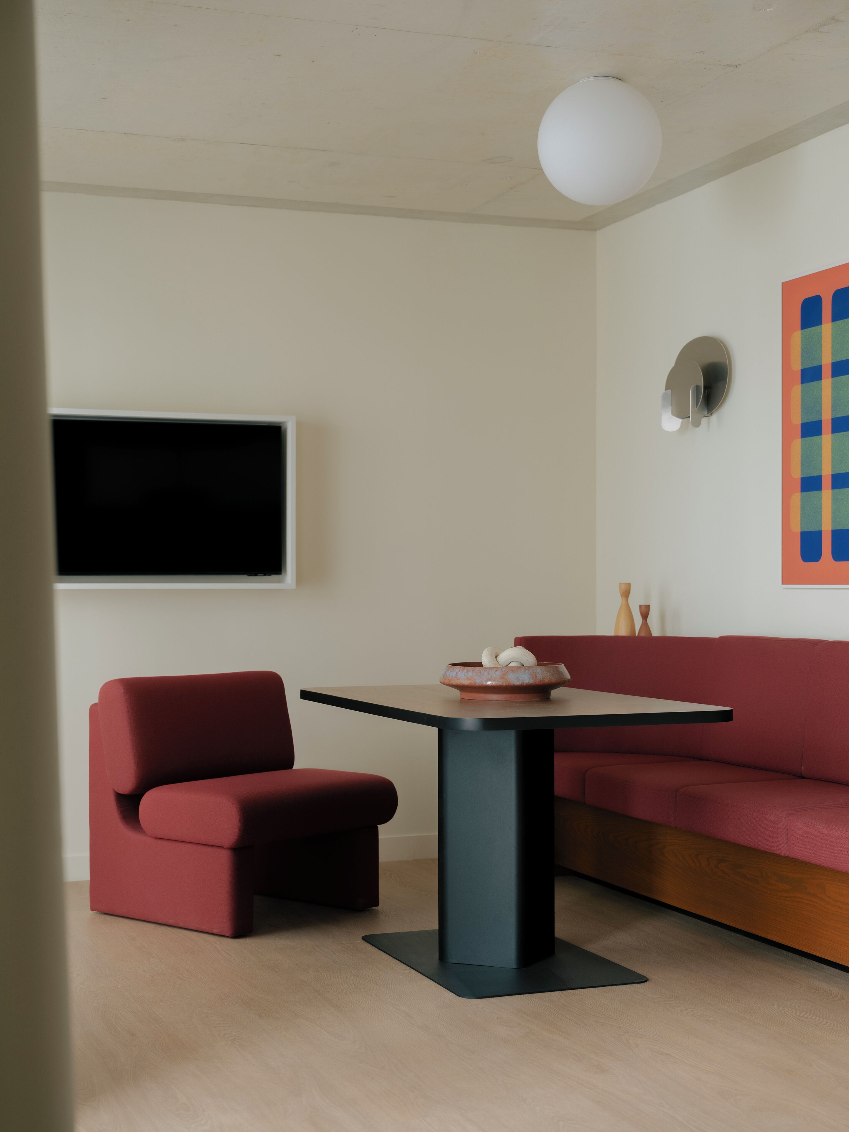 Un salon moderne avec un canapé rouge, une table noire et un téléviseur à écran plat fixé au mur.