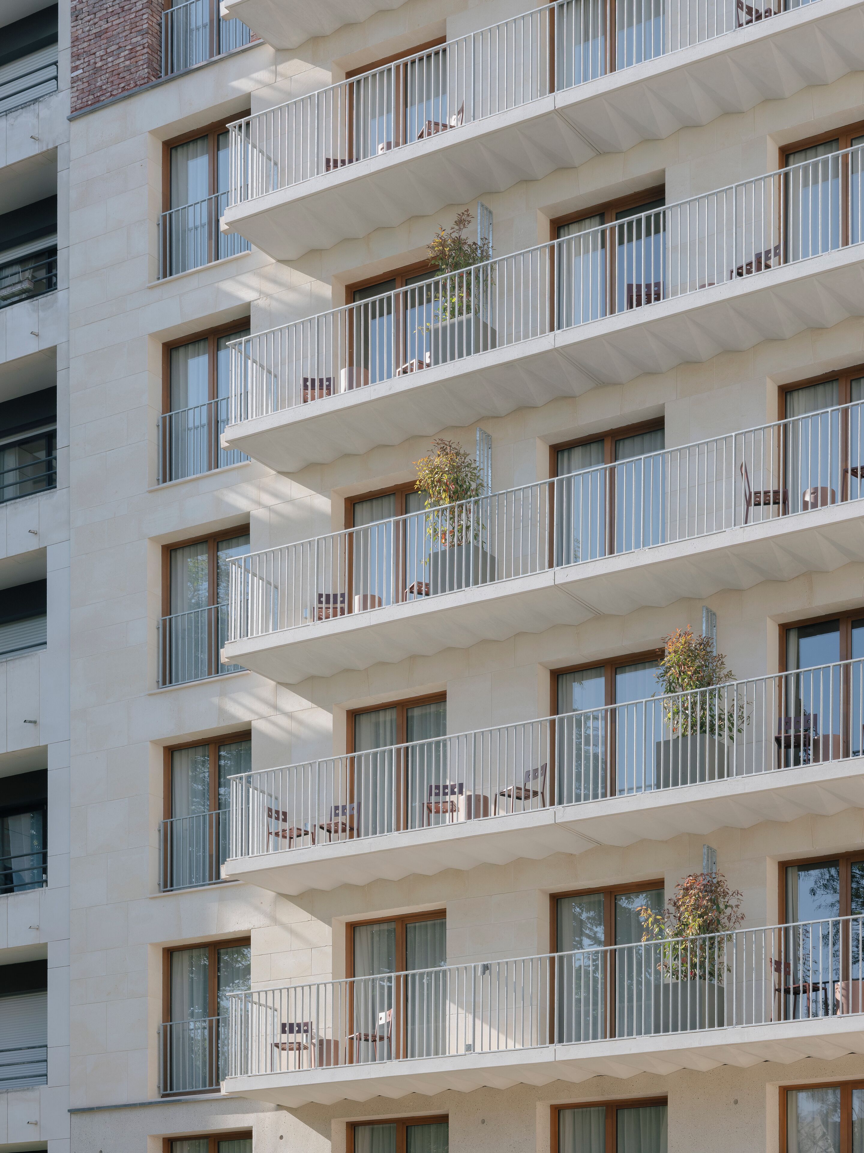 A multi-story building with balconies, each with a metal railing and a potted plant.