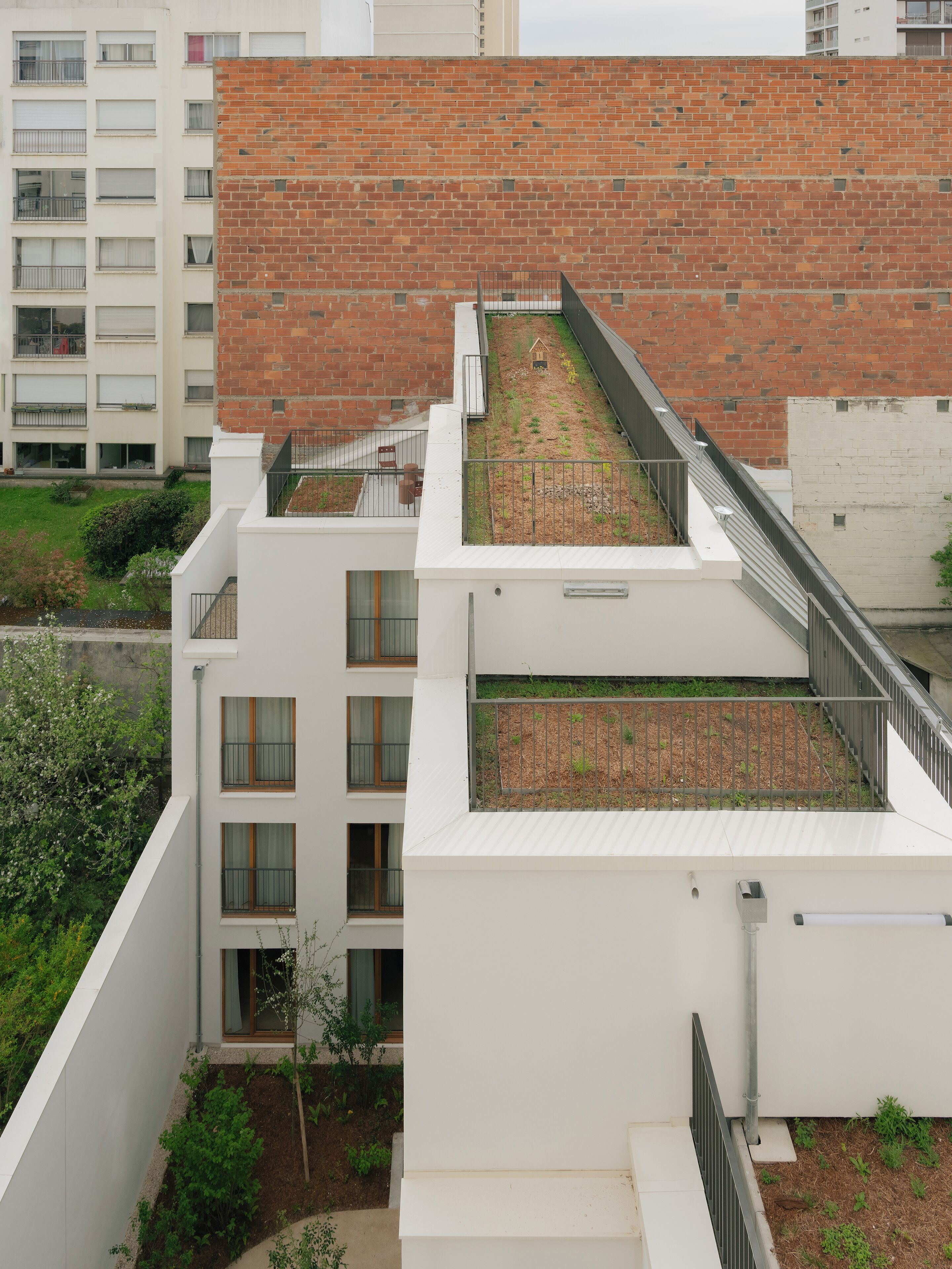 Un edificio moderno con techo plano, varios balcones y una pequeña zona ajardinada.