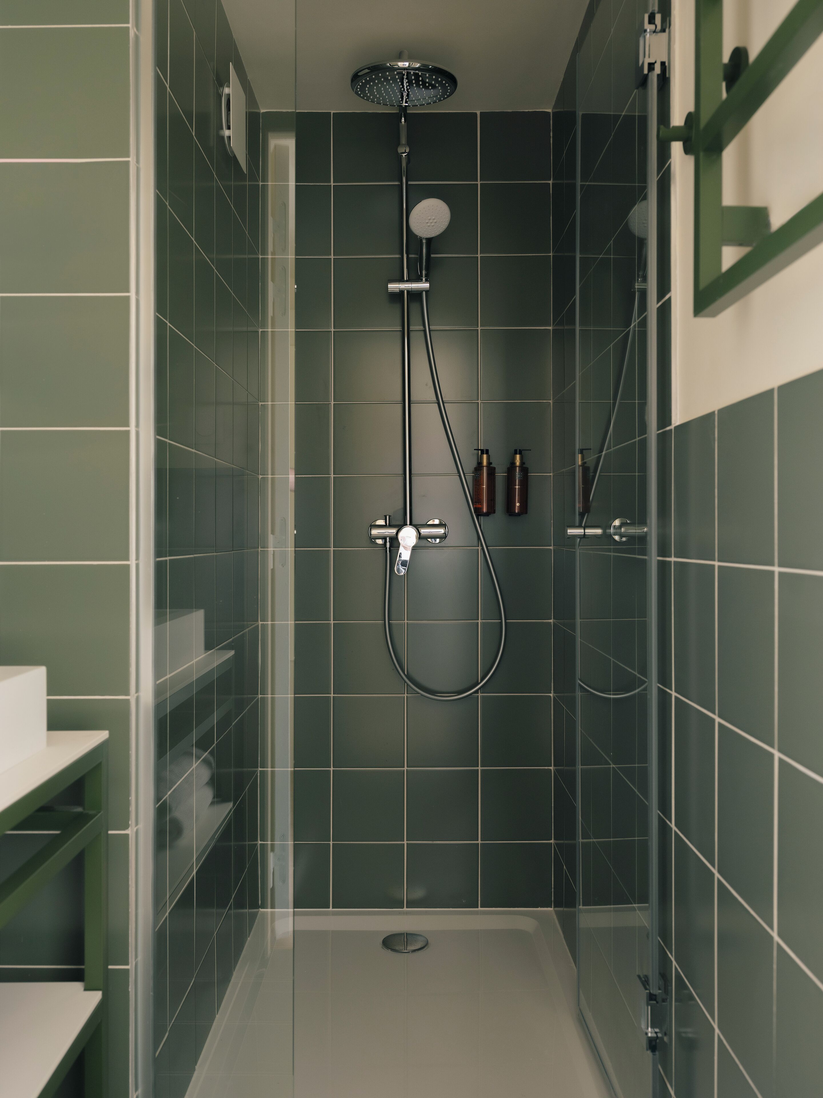 Eine moderne Dusche mit Handbrause und Deckenbrause, eine gläserne Duschkabine und ein weißes Waschbecken links.
