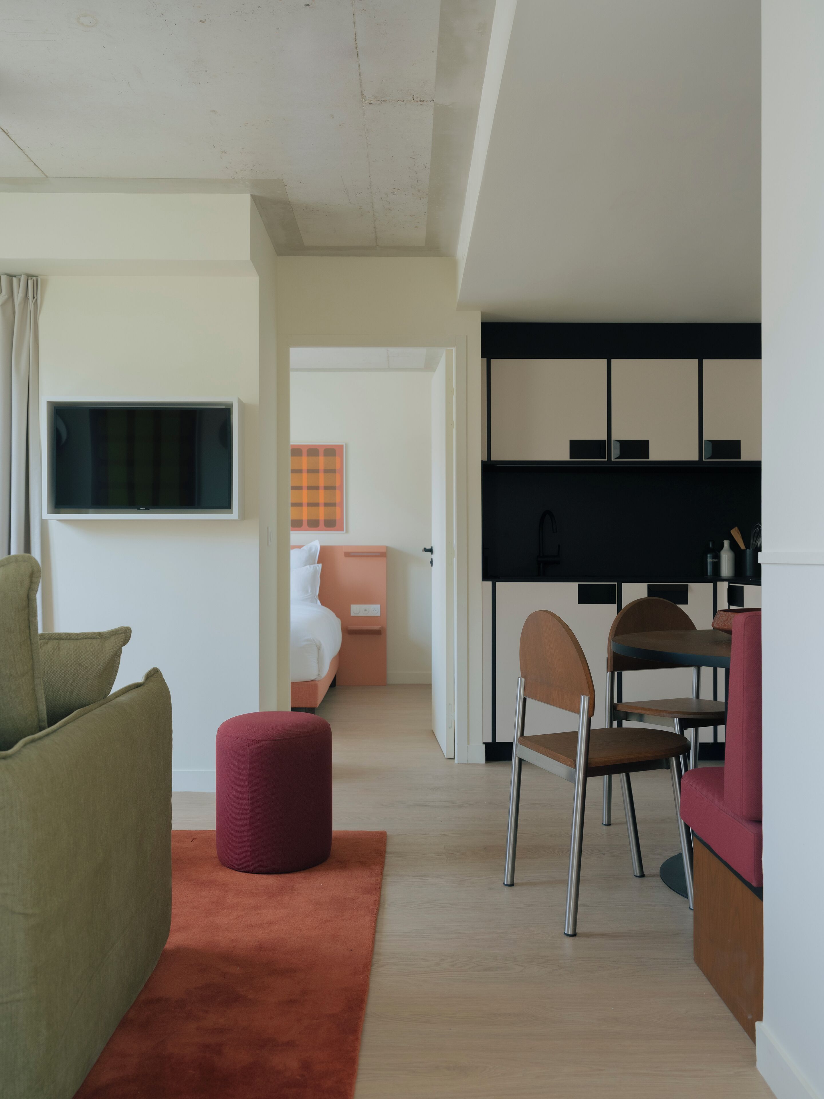 Ein moderner, gut beleuchteter Raum mit einer Couch, Hocker und einem Essbereich mit Stühlen und einem Tisch.