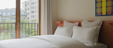 Ett hotellrum med en stor säng, utsikt över byggnader genom fönstret och ett färgstarkt konstverk på väggen.