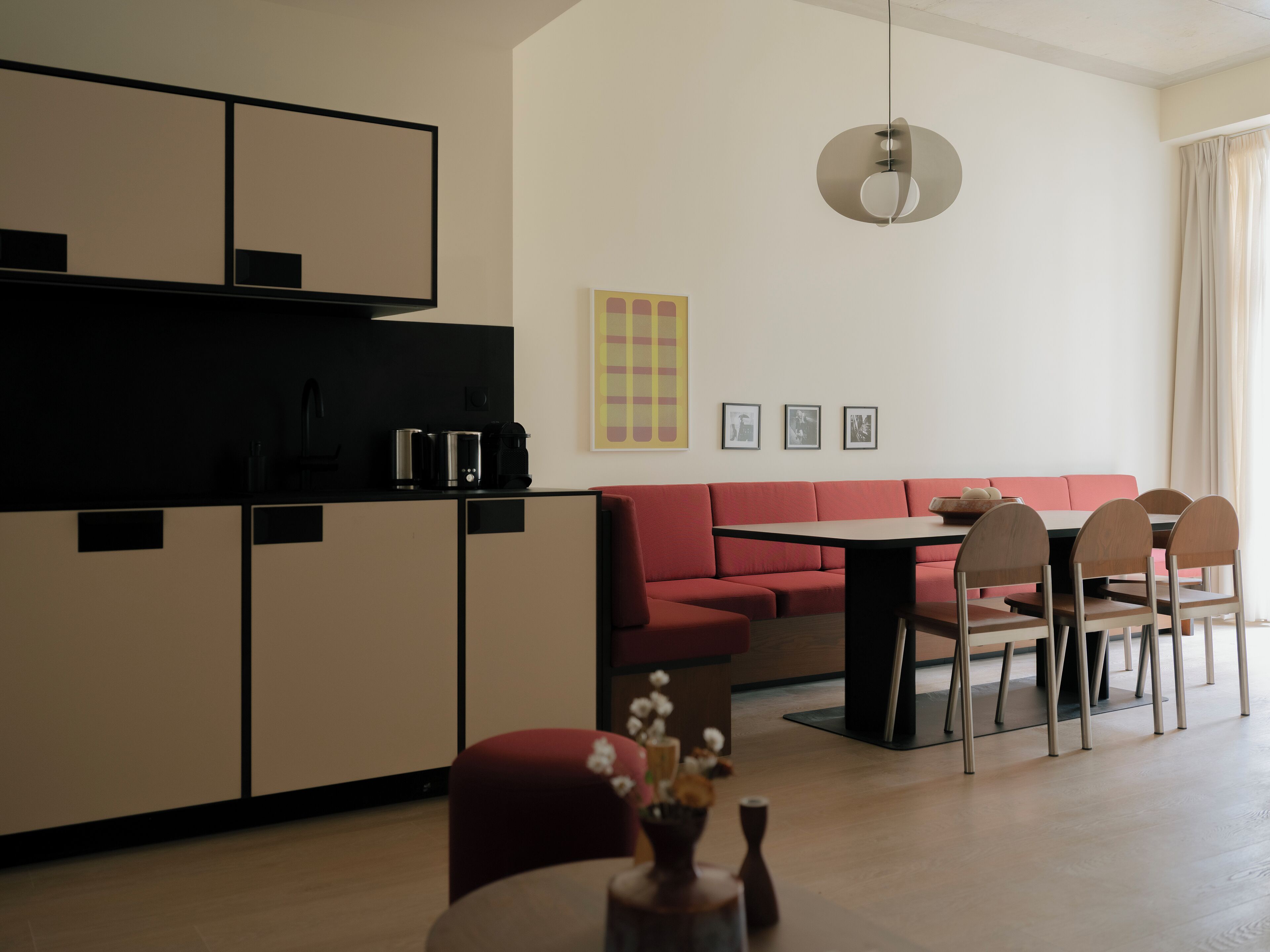A modern kitchen with a dining area, featuring a red sofa, wooden chairs, and a table.