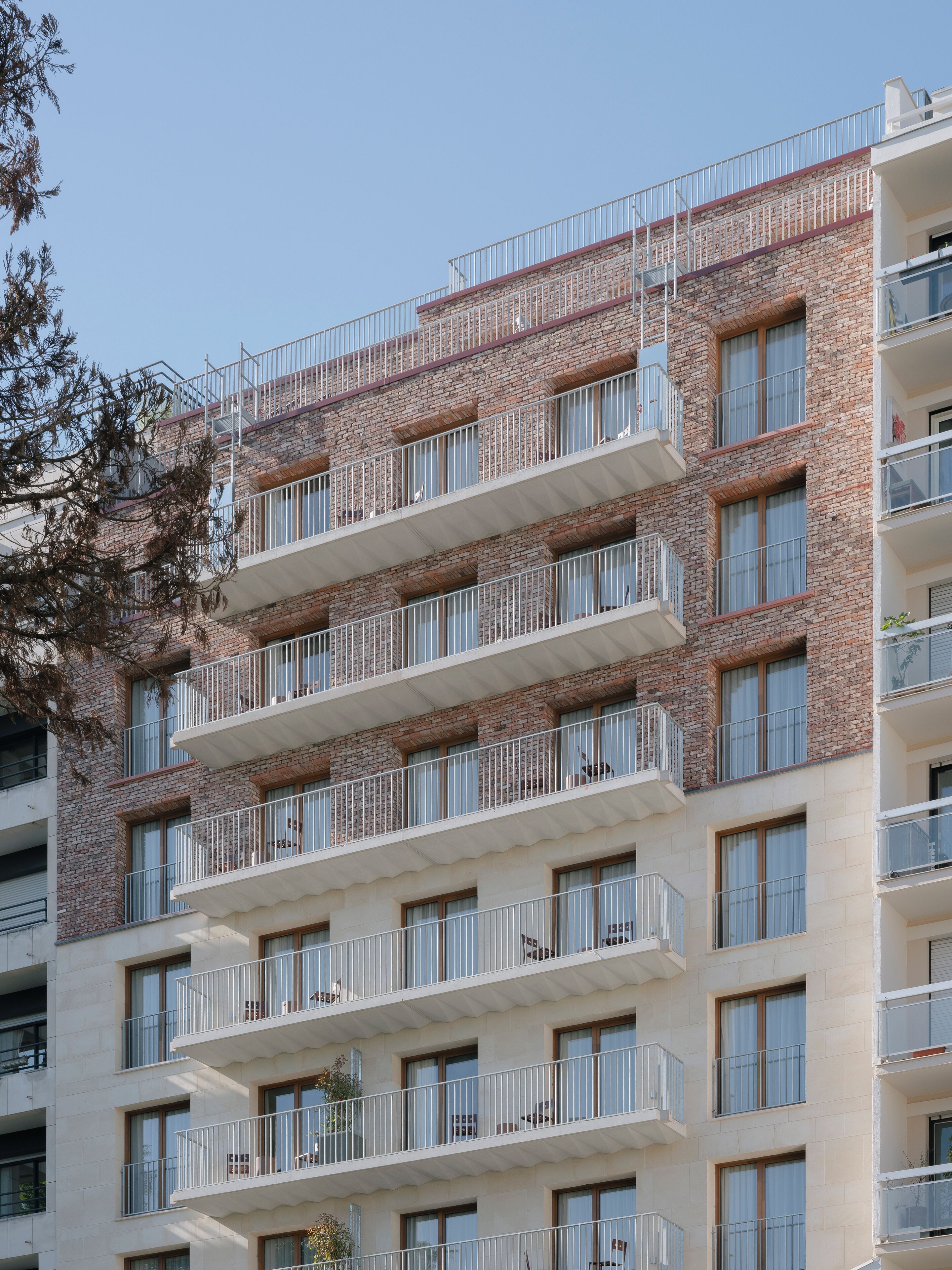 En fleretagers boligbygning med altaner, store vinduer og en murstensfacade.