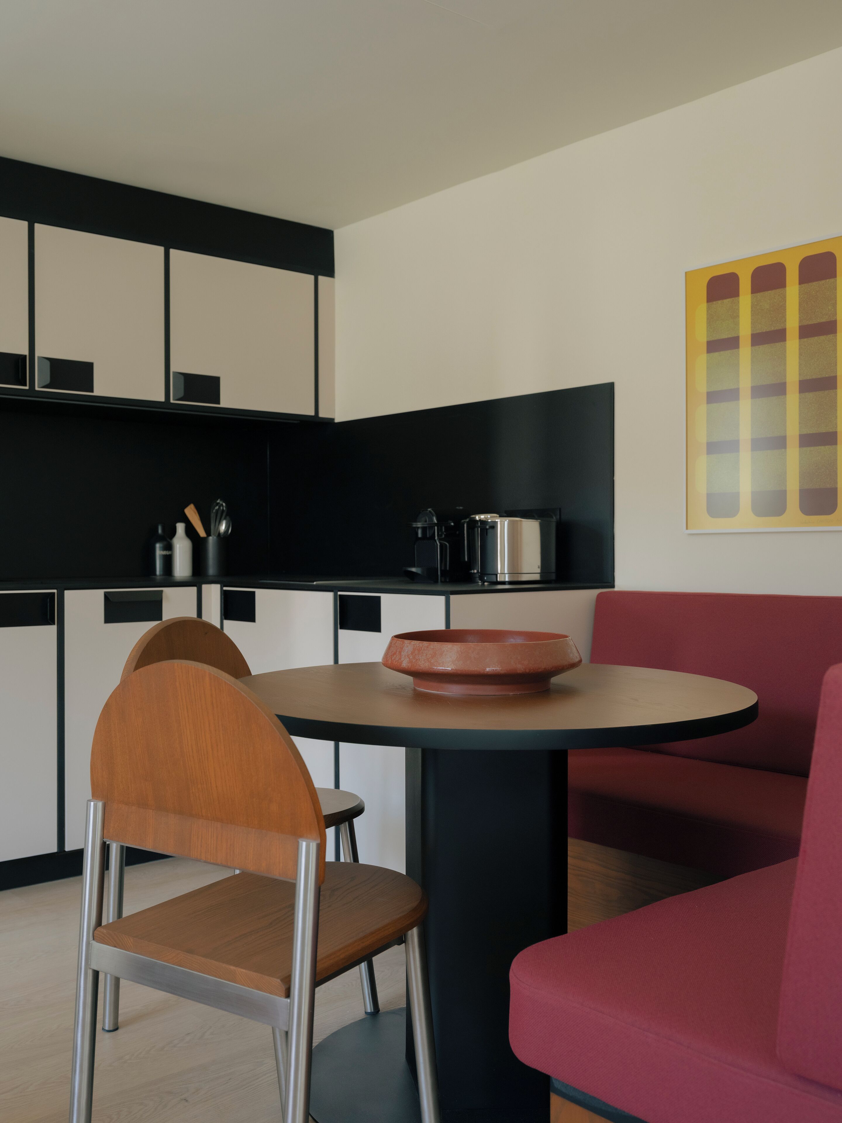 Una cocina moderna con armarios negros, un sofá rojo y una mesa redonda con un bol.