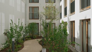 A modern building with multiple windows and balconies, surrounded by a pathway and greenery. - Edgar Suites - Église (Paris)
