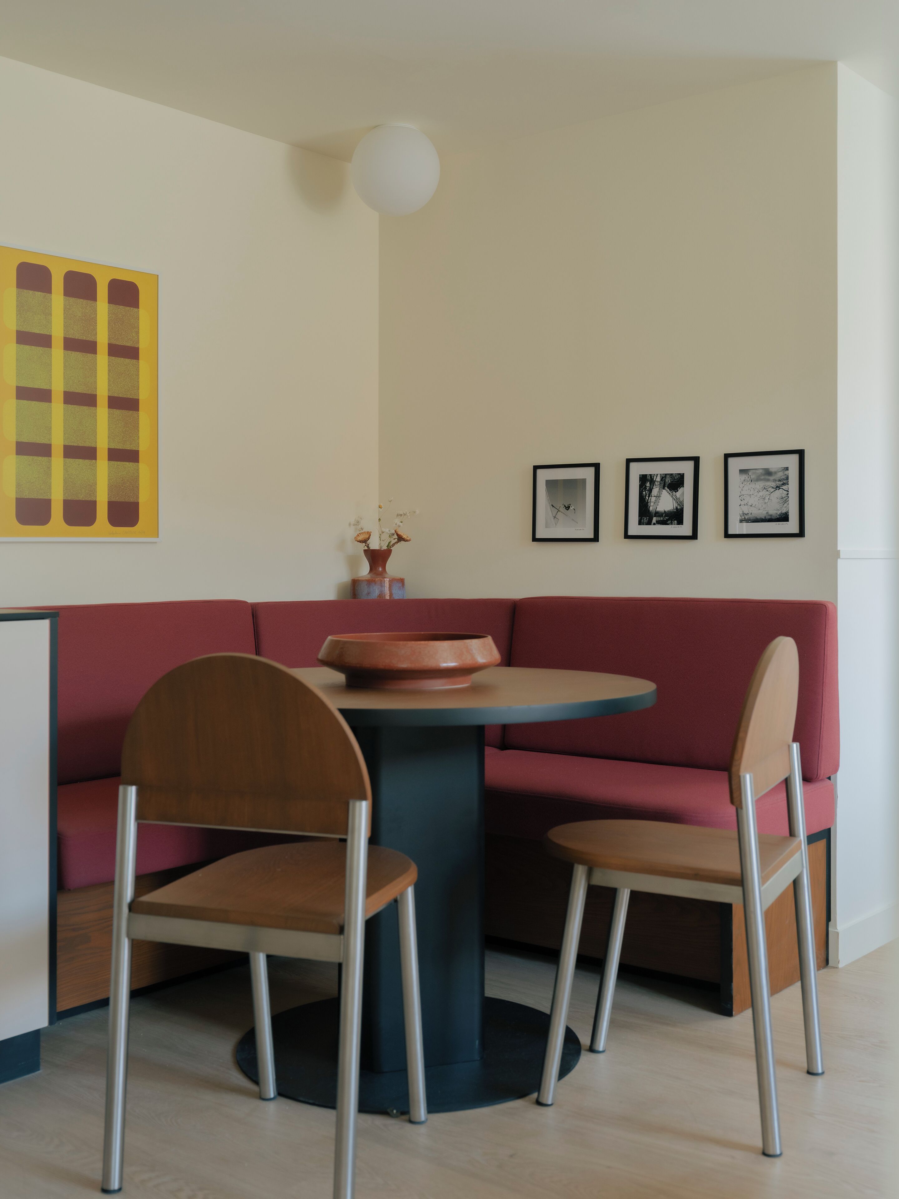 Un coin repas avec une table ronde, deux chaises, un canapé rouge et trois tableaux encadrés accrochés au mur.