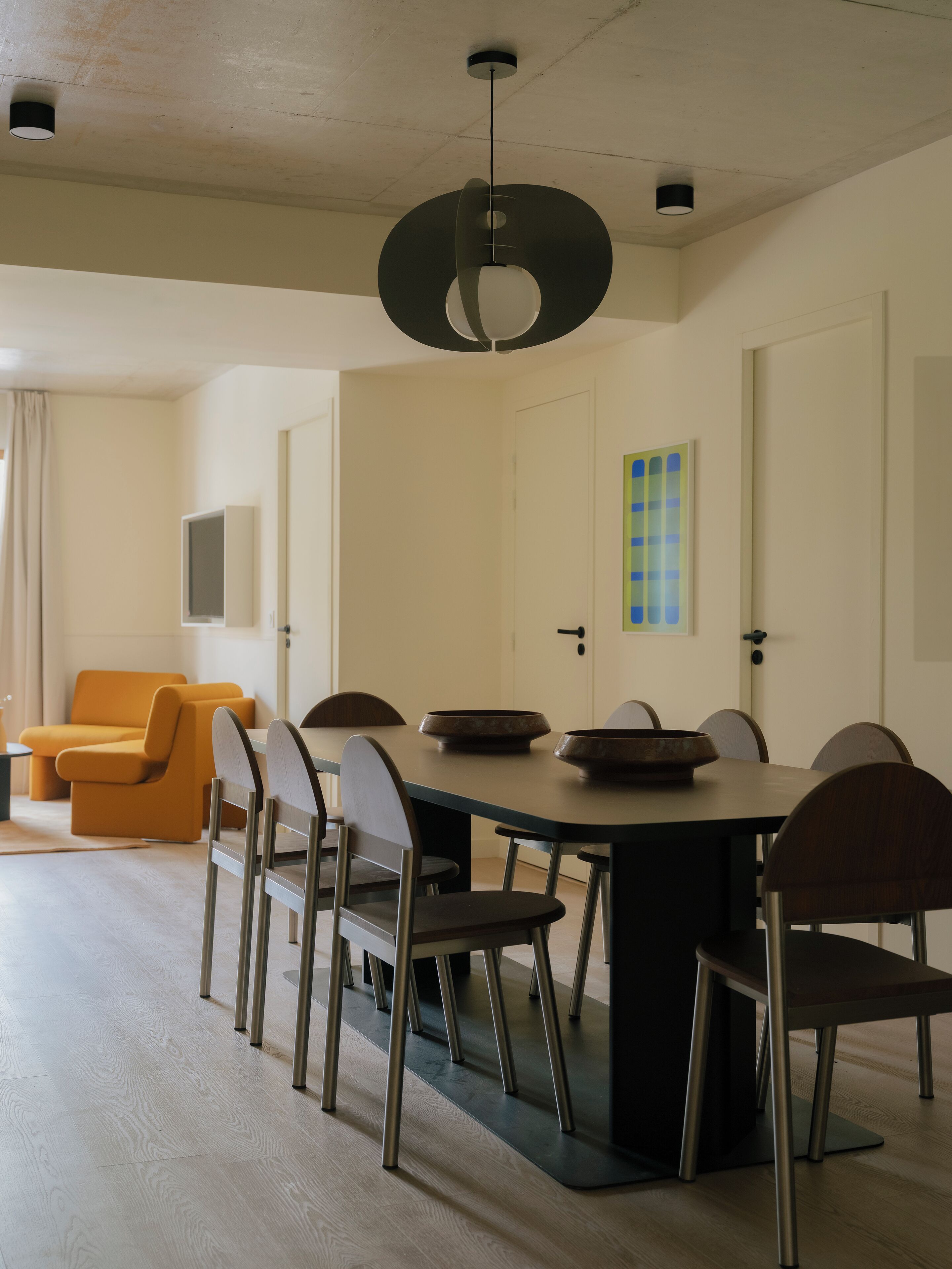 A dining area with a large table, chairs, and a hanging light fixture.