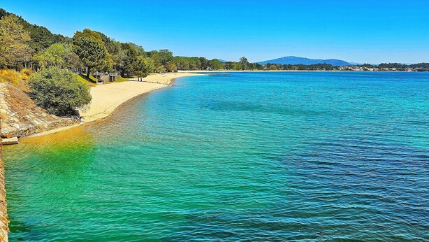 A coastal landscape with a sandy beach, clear turquoise waters, and a backdrop of hills and a mountain. - SeaView Boiro Apartment 2 Bed (Boiro)