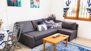 Een woonkamer met een grijze bank, een houten salontafel, een blauw tapijt met patroon en wanddecoratie met een nautisch thema.