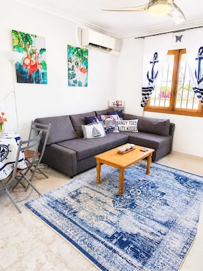 A living room with a gray sofa, a wooden coffee table, a blue patterned rug, and nautical-themed wall art.