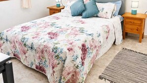 Een slaapkamer met een bed, twee nachtkastjes, een raam met gordijnen en twee ingelijste foto's aan de muur.