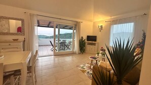 A living room with a dining area, a TV, and a sliding glass door leading to a balcony. - EA WHITE VIBES (Baja Sardinia)