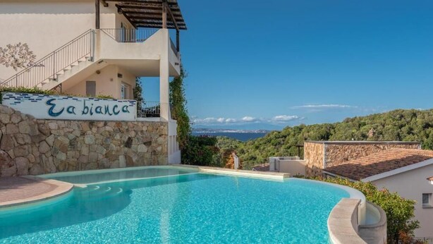 A swimming pool with a stone wall and a sign reading "Eabiana". - EA WHITE VIBES (Baja Sardinia)