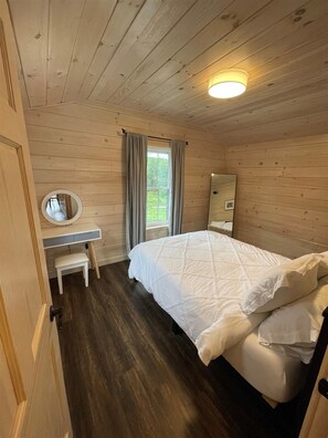 A wooden-paneled bedroom with a bed, a bedside table, a mirror, and a window with curtains.