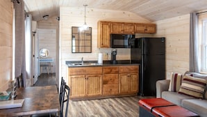 A wooden cabin interior with a kitchen area, dining table, and seating. - FINCH - RESORT WITH 12 PROPERTIES.  NATURAL POND FOR SWIMMING. (SEBAGO)